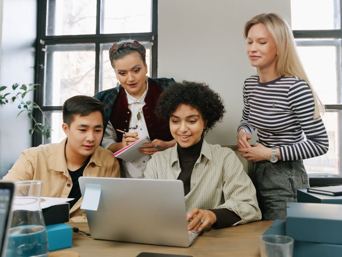 A small team gathered around one laptop, talking through ideas.